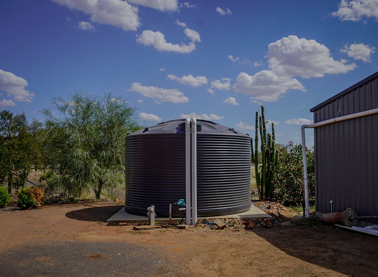 22,500ltr Round Poly Water Tank in Monument Colour installed on a concrete slab by a shed