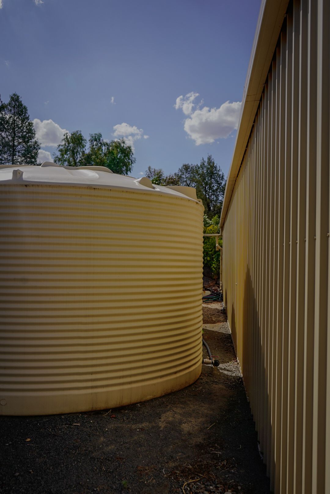 22,500ltr Round Poly Water Tank in Smooth Cream Colour installed beside a Shed